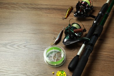 Photo of Fishing rods with spinning reels and baits on wooden background, space for text
