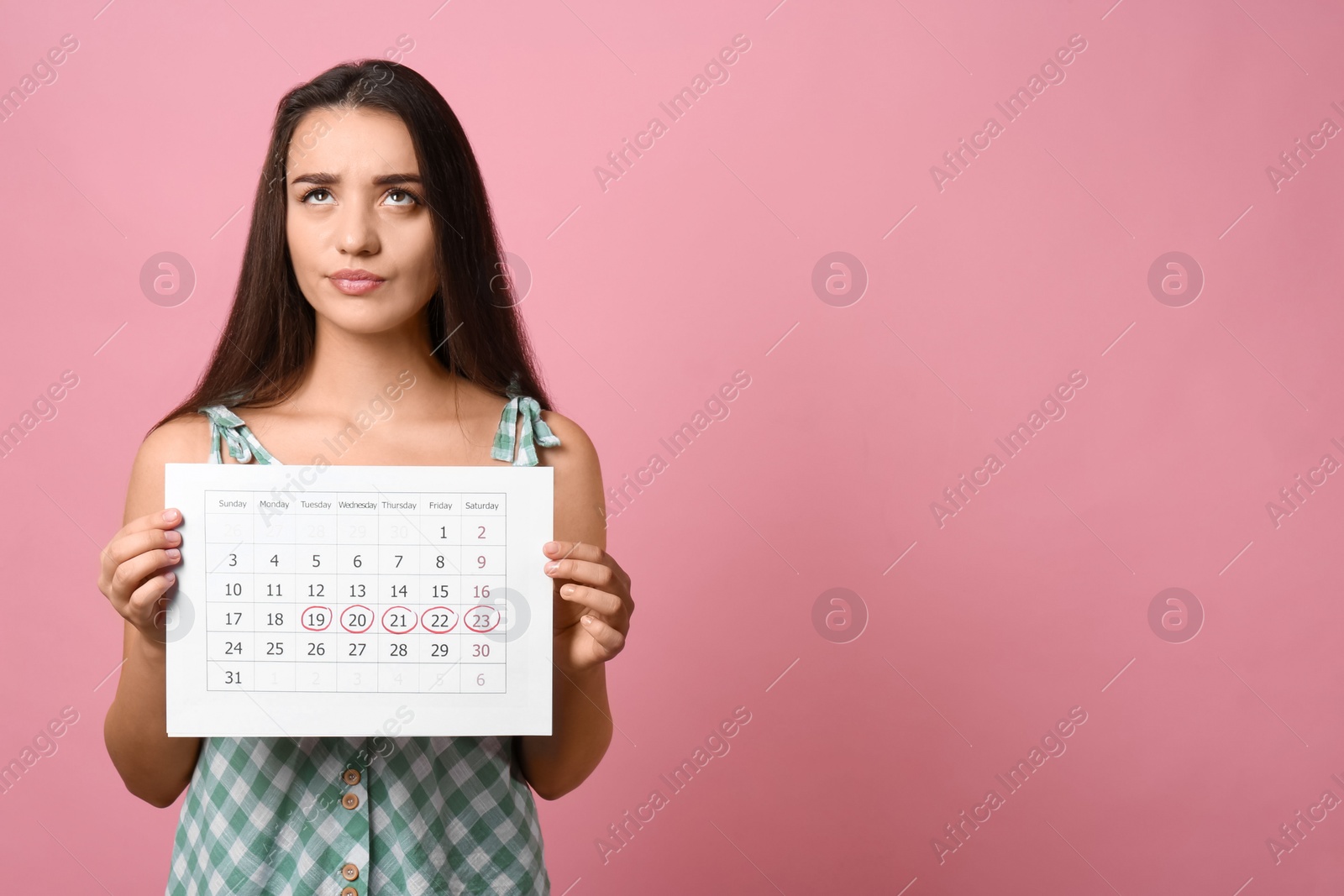 Photo of Young woman holding calendar with marked menstrual cycle days on pink background. Space for text