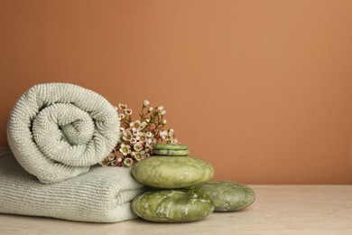Photo of Composition with spa stones, towels and flowers on beige table against brown background. Space for text