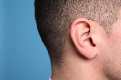 Photo of Man on light blue background, closeup of ear. Space for text