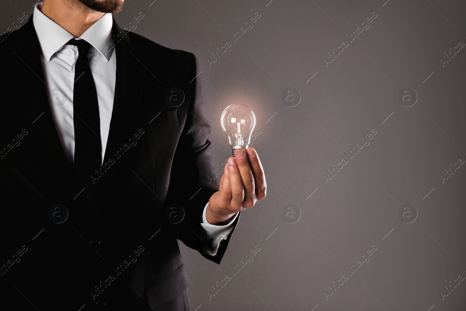 Photo of Businessman holding lamp bulb against gray background, closeup. Space for text