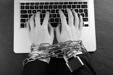 Image of Top view of woman with chained hands using laptop at dark table, black and white effect. Internet addiction