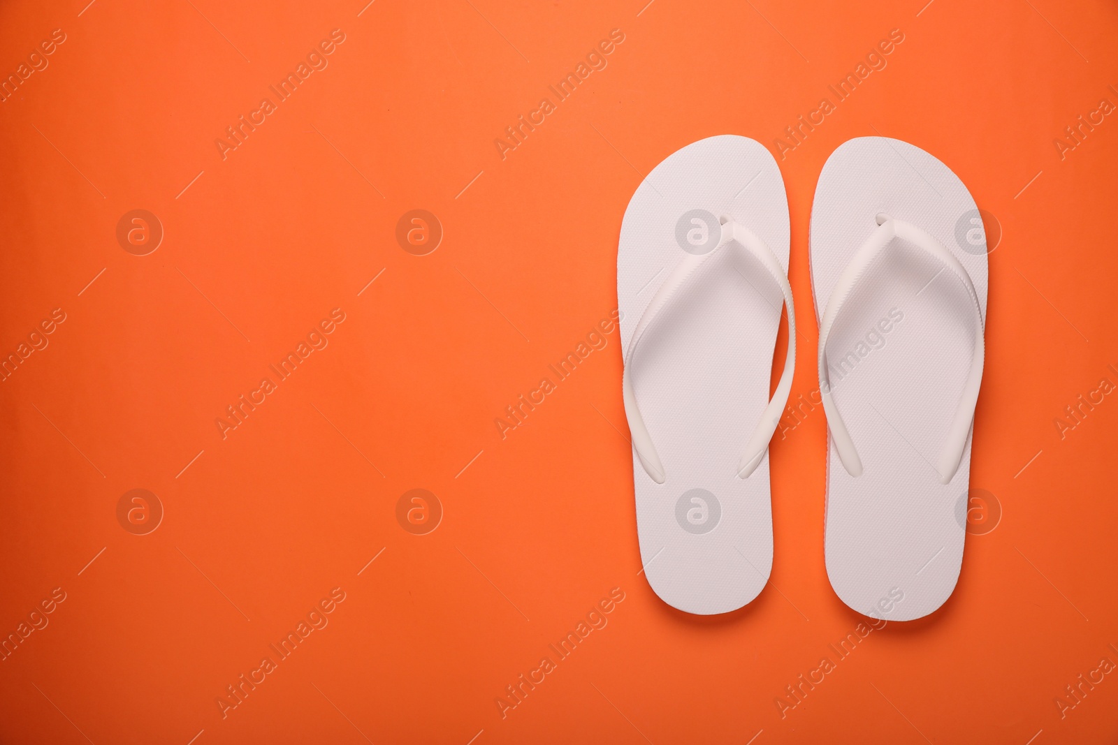 Photo of Stylish white flip flops on orange background, top view. Space for text