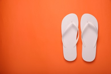 Stylish white flip flops on orange background, top view. Space for text