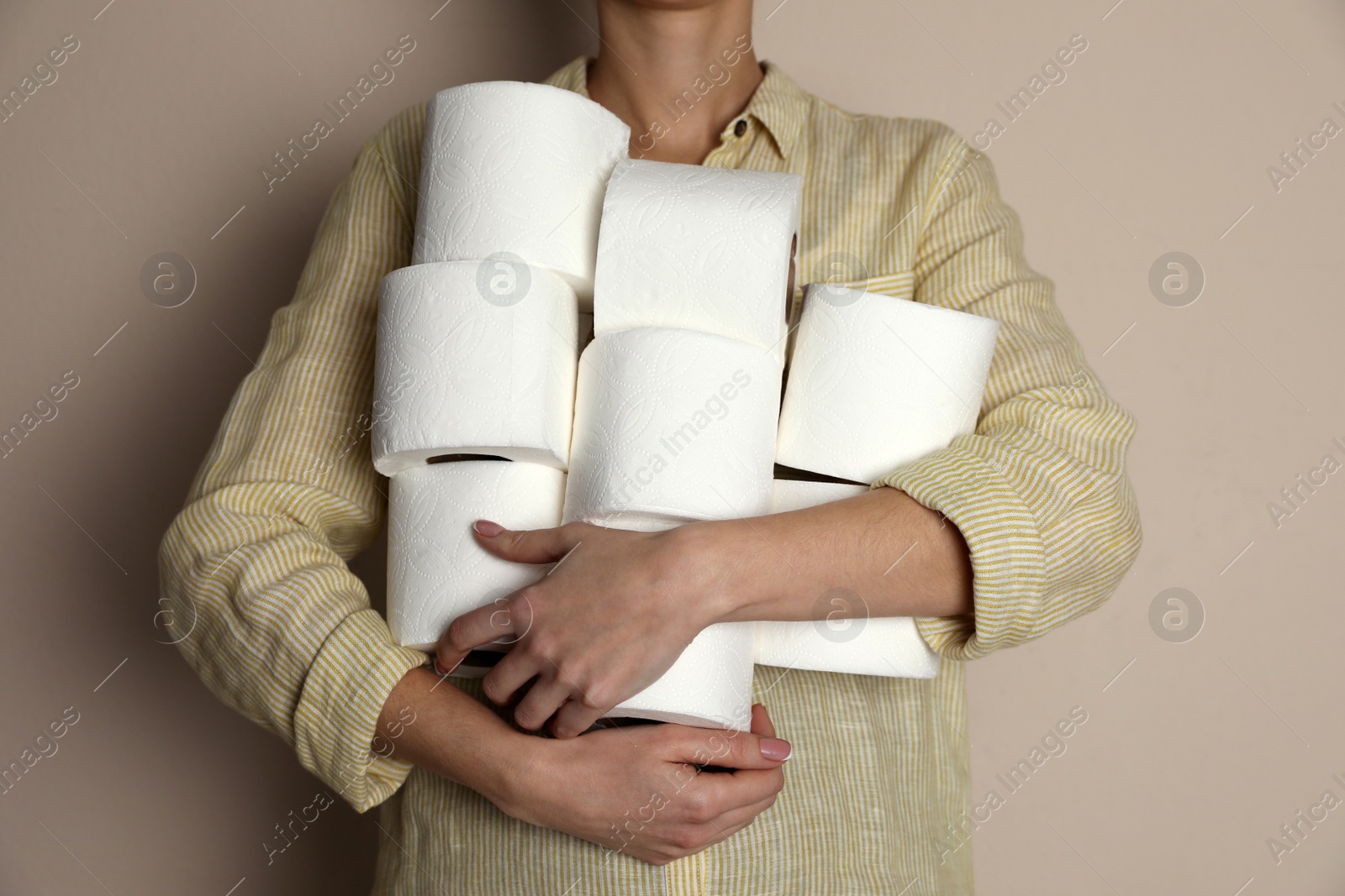 Photo of Woman with heap of toilet paper rolls on beige background, closeup