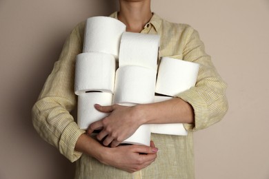 Photo of Woman with heap of toilet paper rolls on beige background, closeup