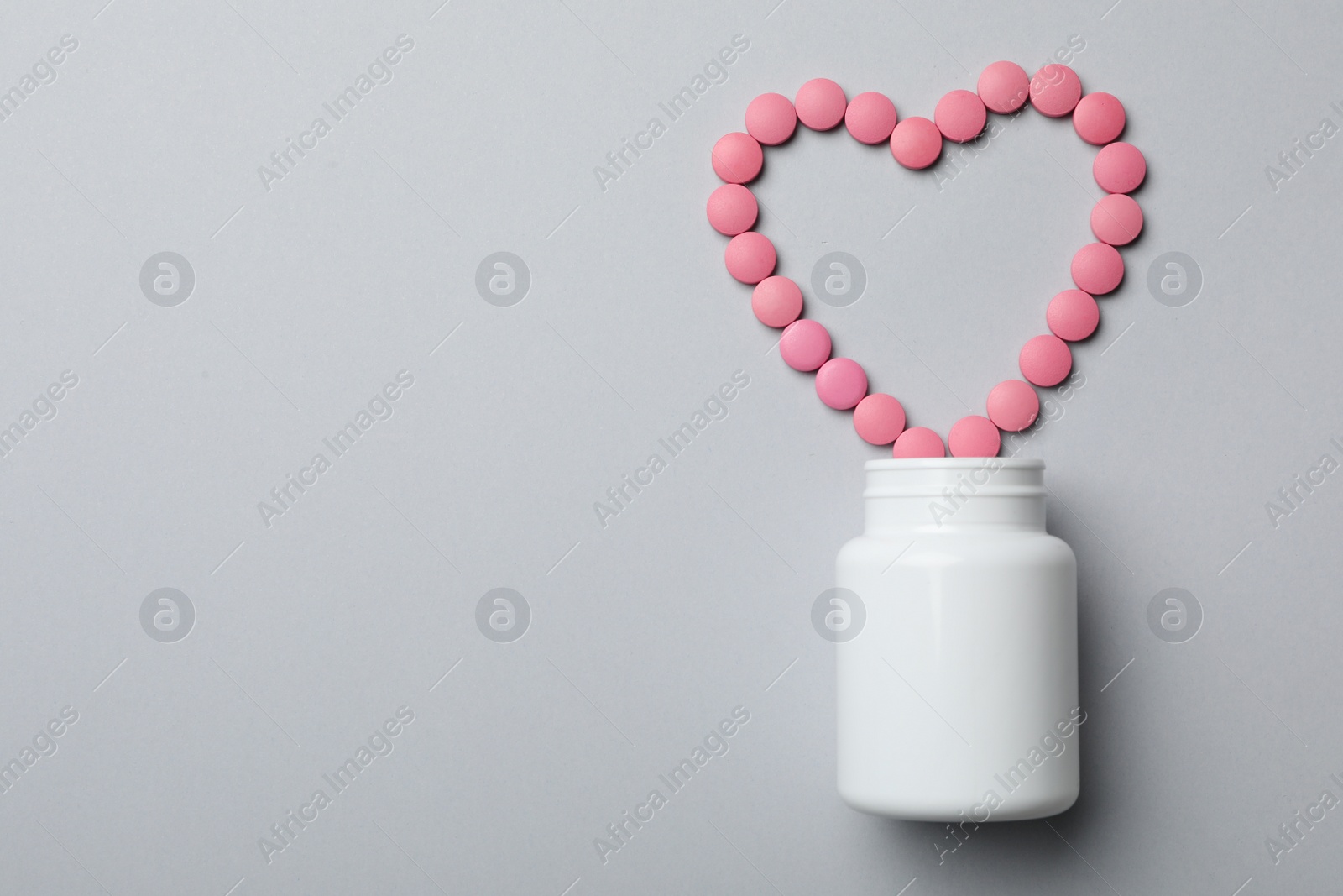 Photo of Bottle and heart of pills on grey background, flat lay. Space for text