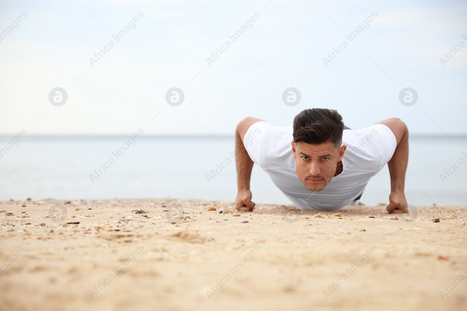 Photo of Muscular man doing push up on beach, space for text. Body training