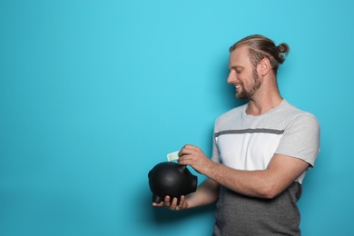 Man putting money into piggy bank on color background. Space for text