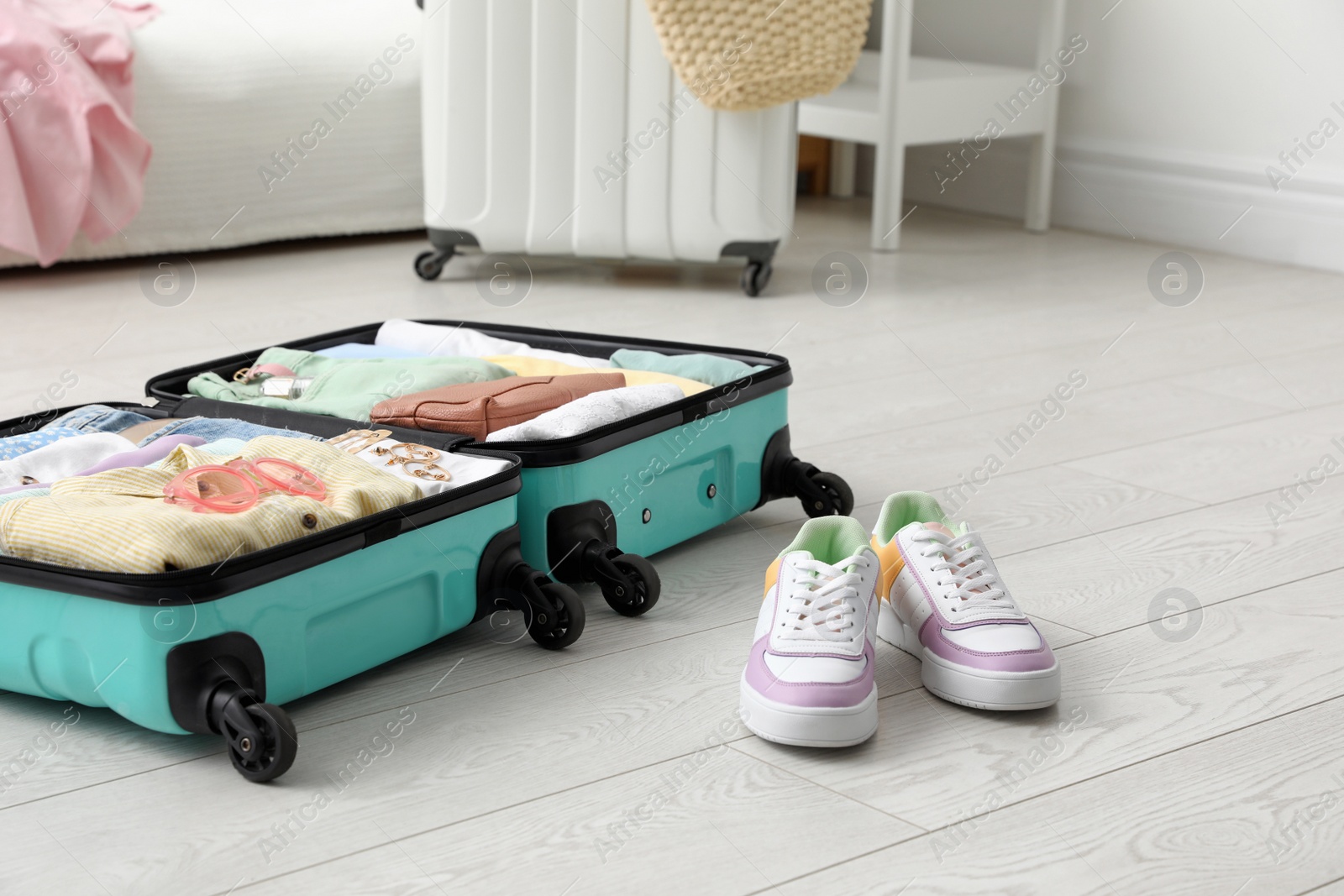 Photo of Open suitcase packed for trip and shoes on floor in room