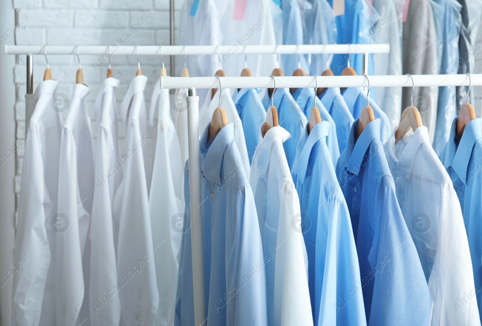 Photo of Rack with clean clothes on hangers after dry-cleaning indoors