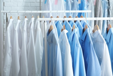 Photo of Rack with clean clothes on hangers after dry-cleaning indoors