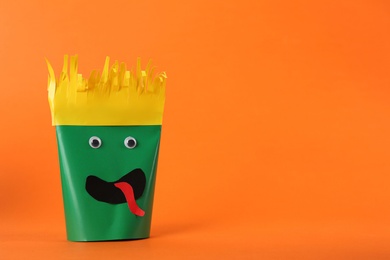 Photo of Funny green monster on orange background, space for text. Halloween decoration