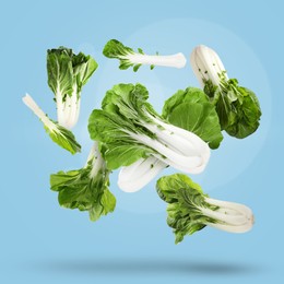 Fresh green pak choy cabbages falling on light blue background