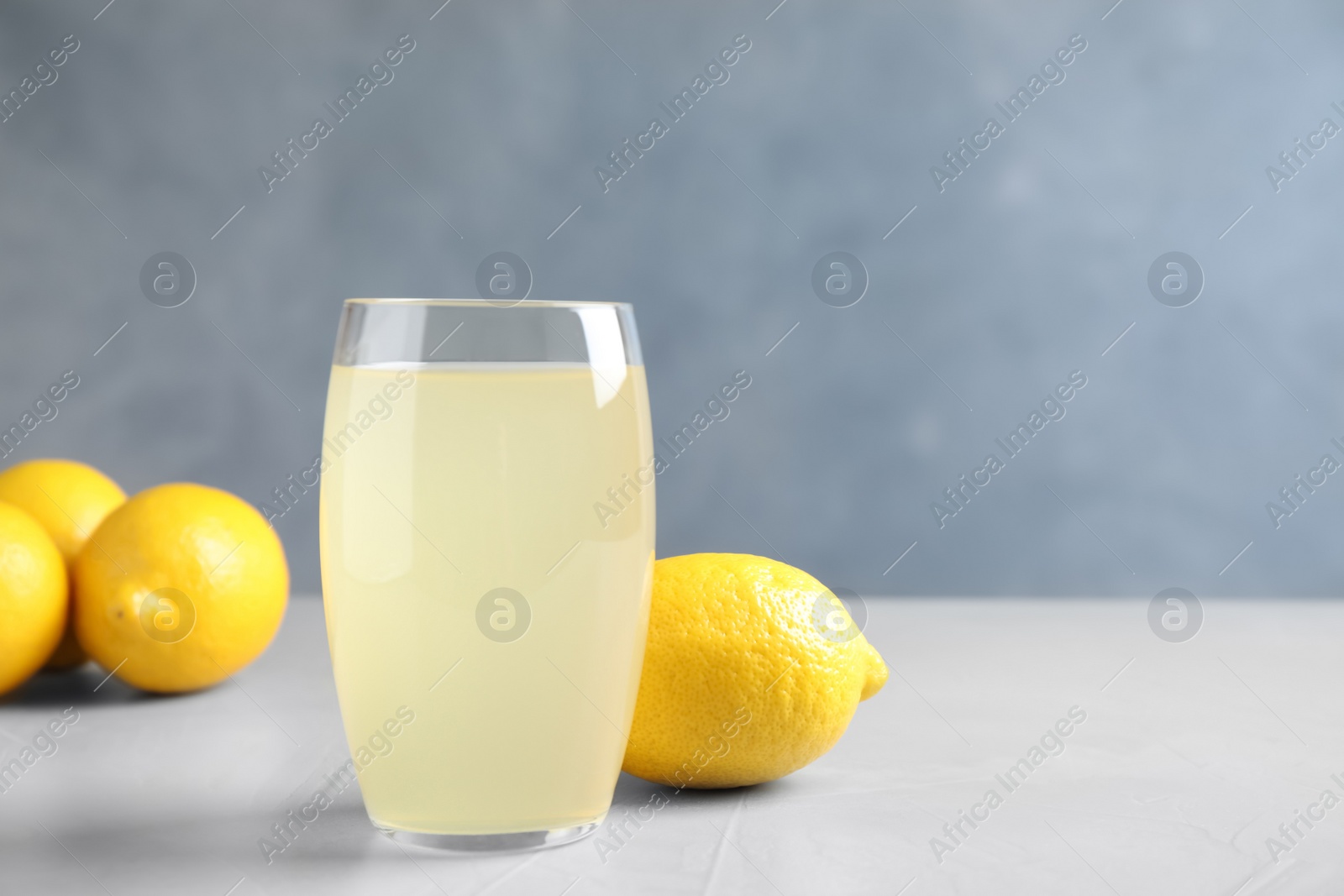 Photo of Glass of lemonade and fresh fruits on light table. Space for text