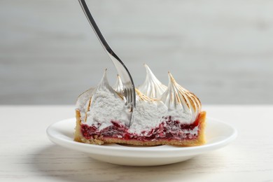 Photo of Eating tasty tartlet with meringue and jam on white table, closeup. Delicious dessert
