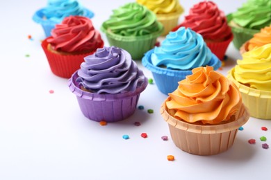 Photo of Many tasty cupcakes with bright cream and sprinkles on white background, closeup