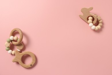 Photo of Baby accessories. Wooden rattles and teether on pink background, flat lay. Space for text