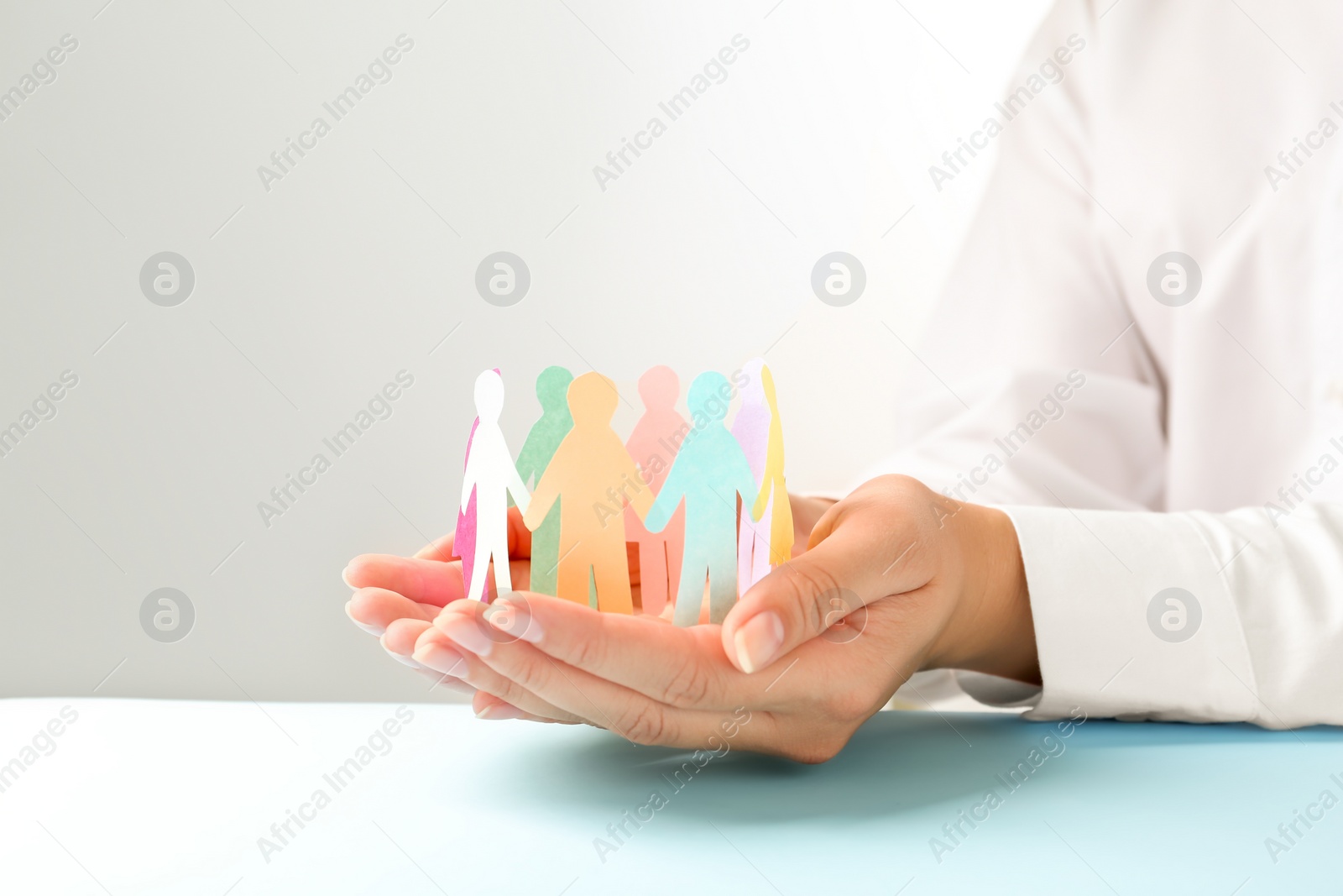 Photo of Woman holding paper human figures at light table against grey background, closeup. Diversity and inclusion concept