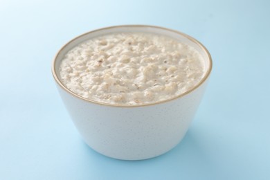 Photo of Tasty boiled oatmeal in bowl on light blue table, closeup