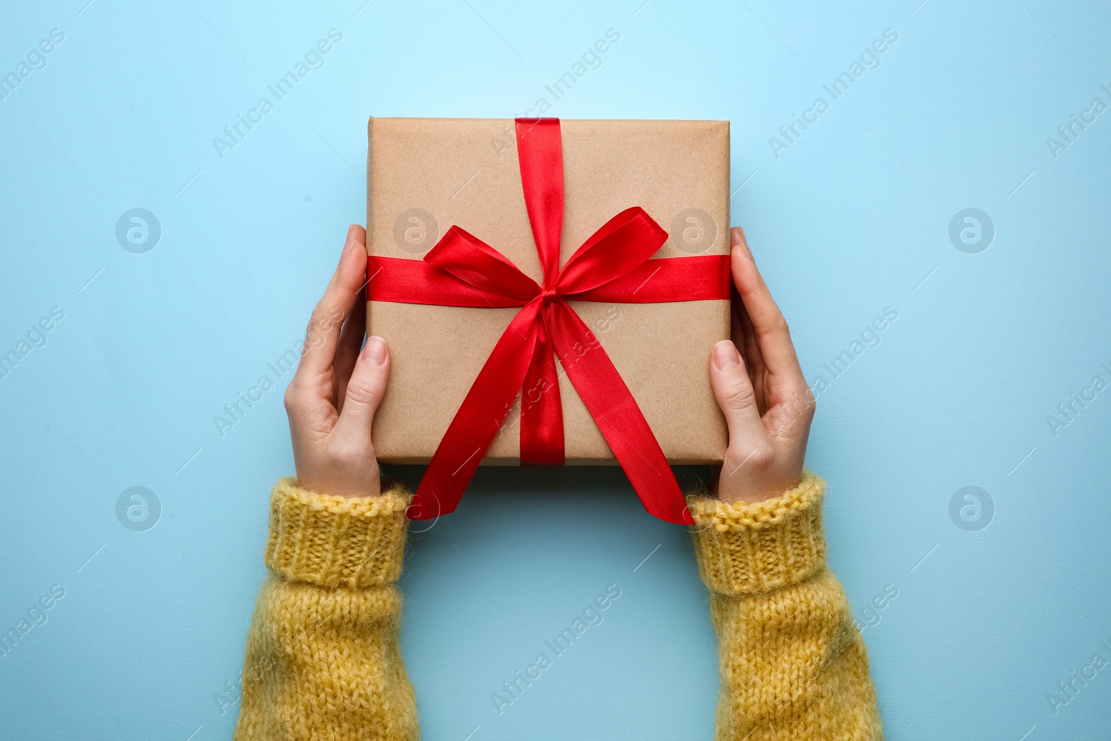 Photo of Woman holding Christmas gift box on light blue background, top view