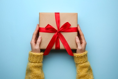 Woman holding Christmas gift box on light blue background, top view