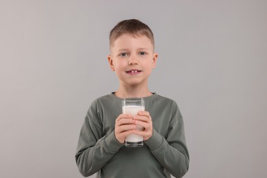 Cute boy with glass of fresh milk on light grey background