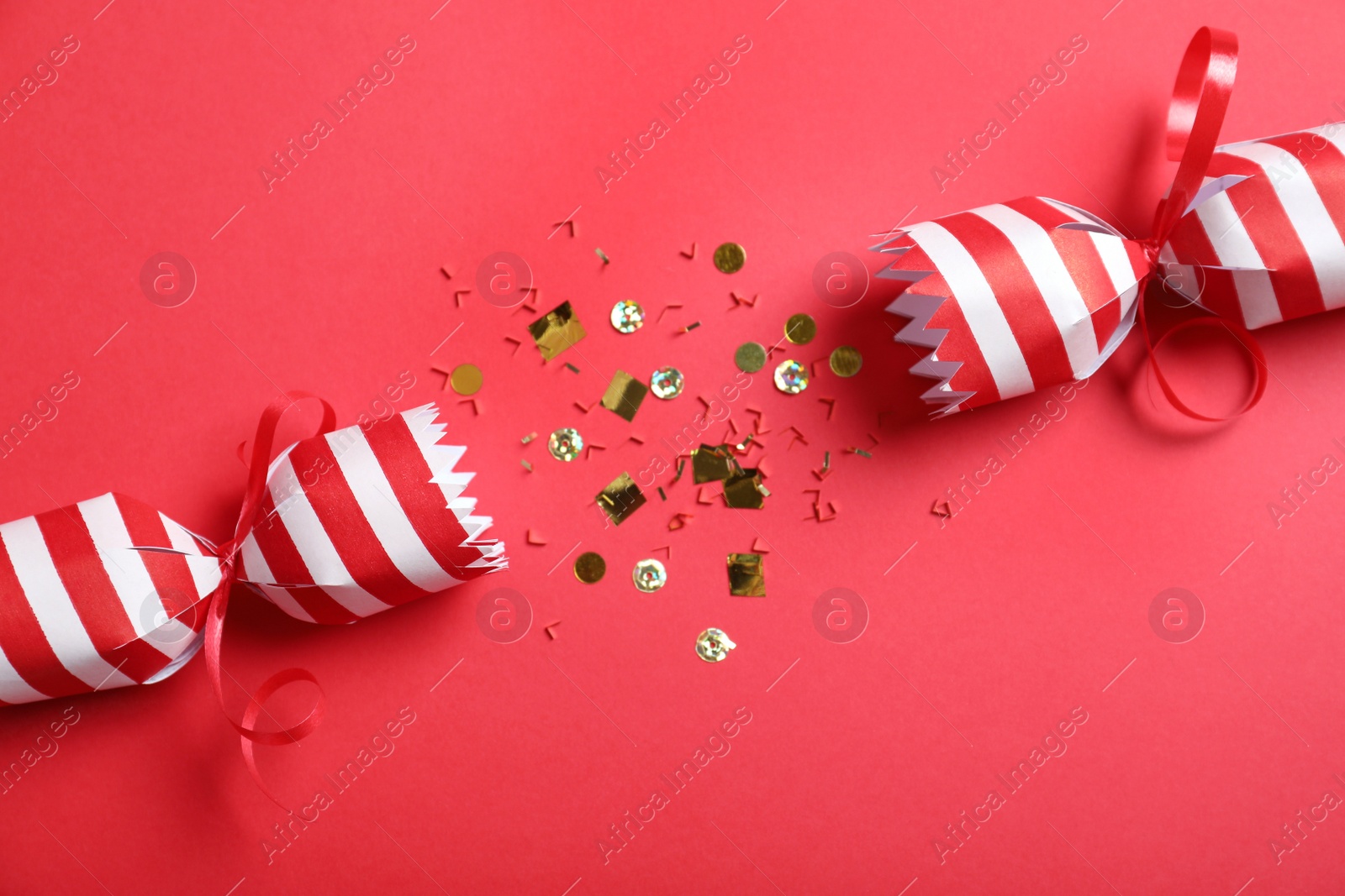 Photo of Open Christmas cracker with shiny confetti on red background, top view