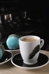 Photo of Cup of fresh aromatic coffee and delicious macarons on wooden counter in cafe