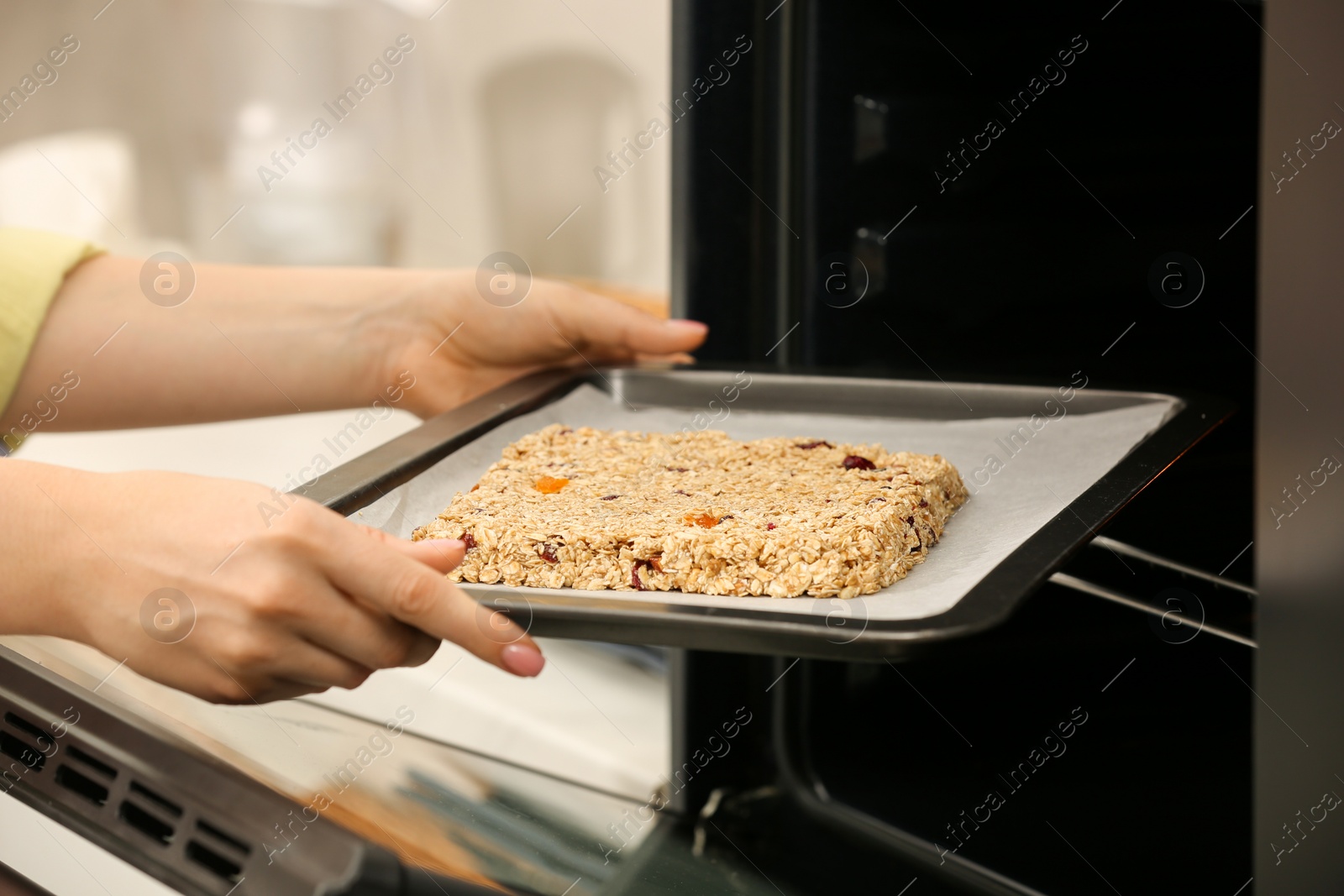 Photo of Making granola. Woman putting baking tray into oven in kitchen, closeup