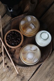 Photo of Refreshing iced coffee with milk in glasses, ingredients and straws on wooden table, flat lay