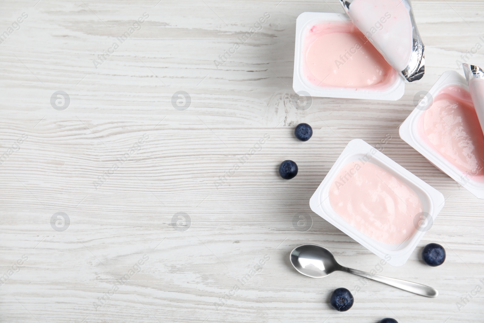 Photo of Plastic cups with tasty yogurts and blueberries on white wooden table, flat lay. Space for text