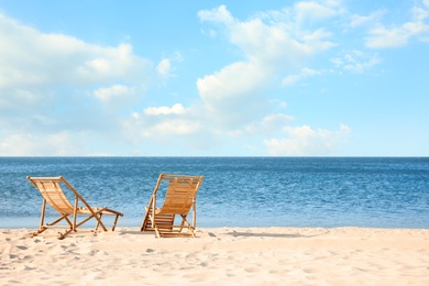 Wooden deck chairs on sandy beach near sea