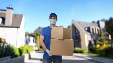 Image of Courier in protective mask and gloves with boxes on street. Delivery service during coronavirus quarantine
