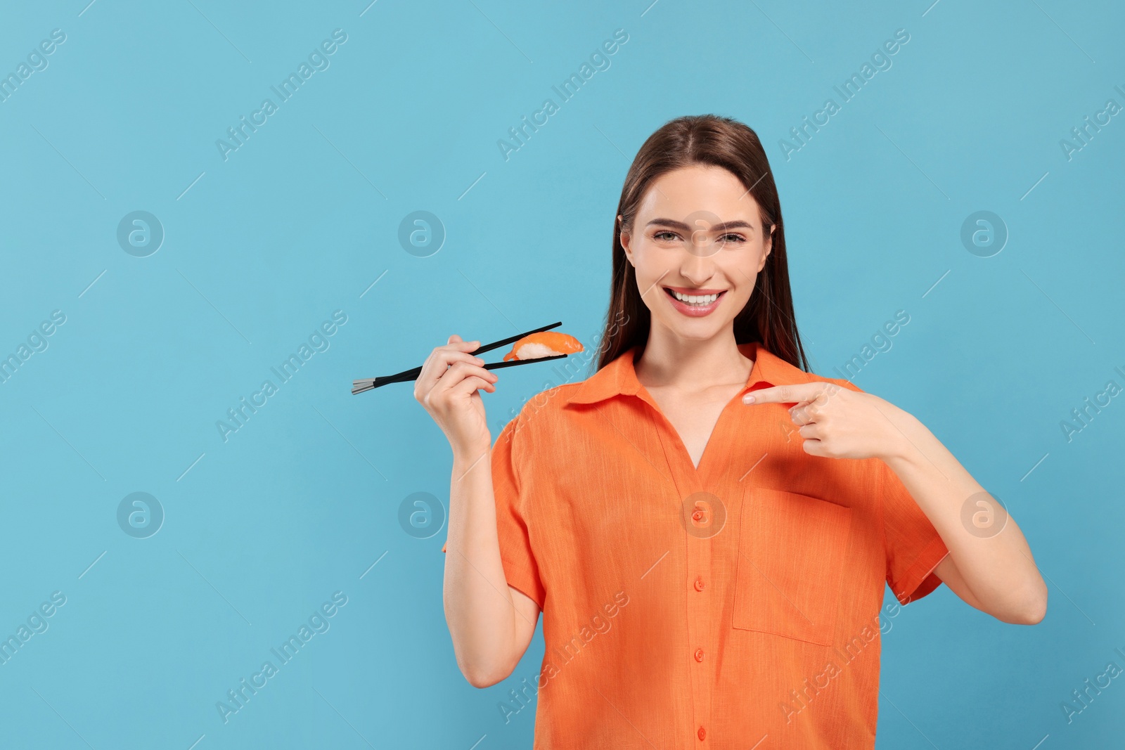 Photo of Happy beautiful young woman holding sushi with chopsticks on light blue background. Space for text