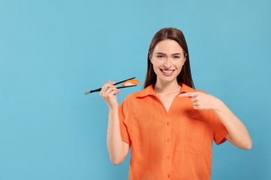 Photo of Happy beautiful young woman holding sushi with chopsticks on light blue background. Space for text