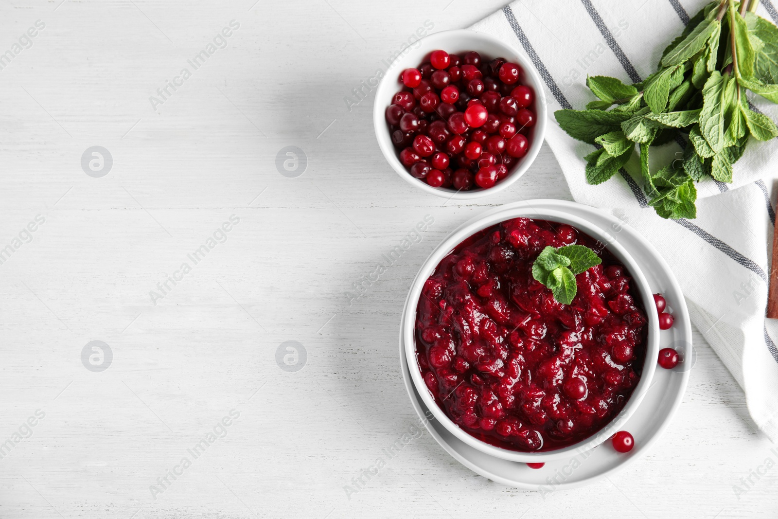 Photo of Flat lay composition with cranberry sauce in bowl on white wooden background. Space for text