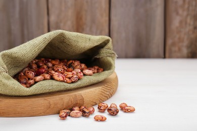 Photo of Overturned sack with dry kidney beans on white wooden table, closeup. Space for text