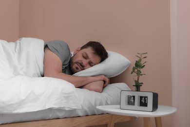 Man sleeping in bed and alarm clock on nightstand at home