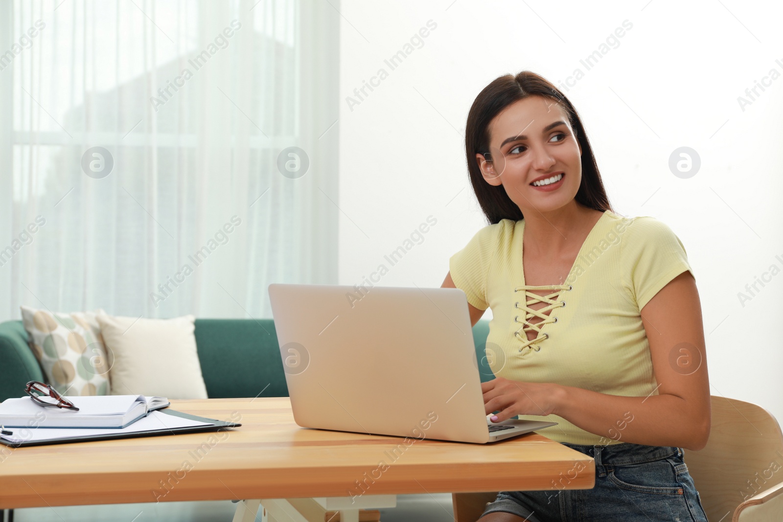 Photo of Young woman using laptop at table in living room. Internet shopping