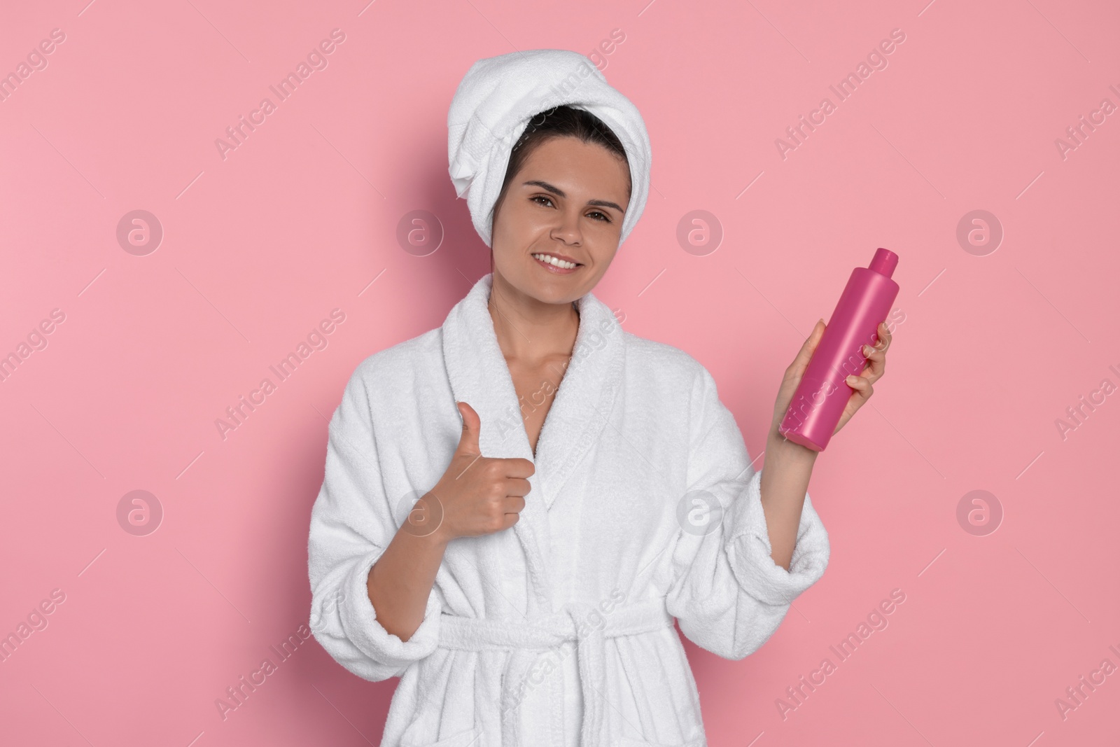 Photo of Beautiful young woman holding bottle of shampoo on pink background