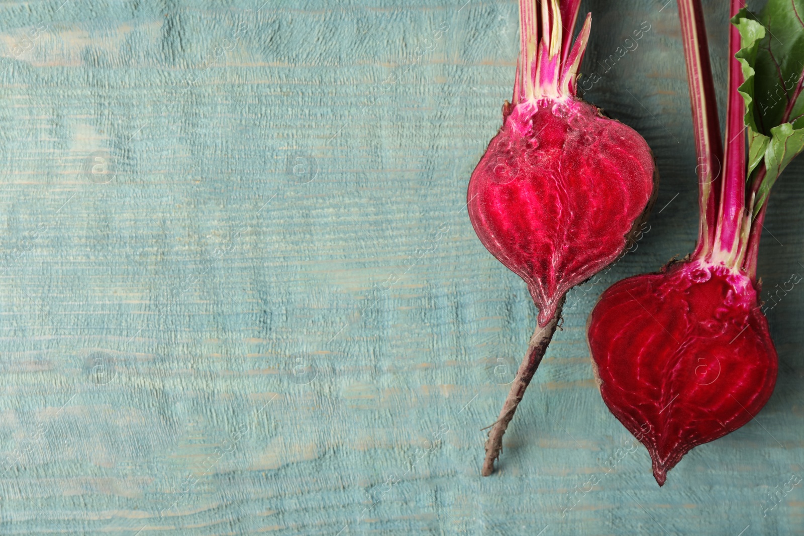 Photo of Halves of raw beet on blue wooden table, flat lay. Space for text