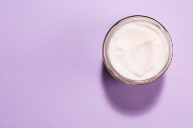 Glass jar of face cream on violet background, top view. Space for text