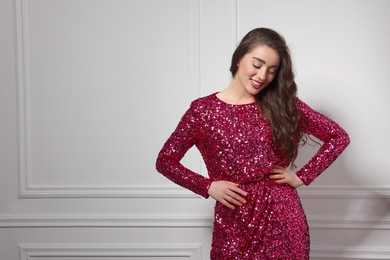 Photo of Beautiful young woman in stylish pink sequin dress near white wall indoors, space for text. Party outfit