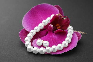 Photo of Elegant pearl earrings, bracelet and orchid flower on black background, closeup