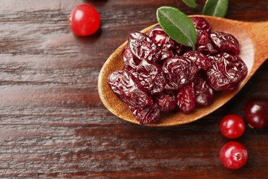 Tasty dried cranberries in spoon and fresh ones on wooden table, top view. Space for text