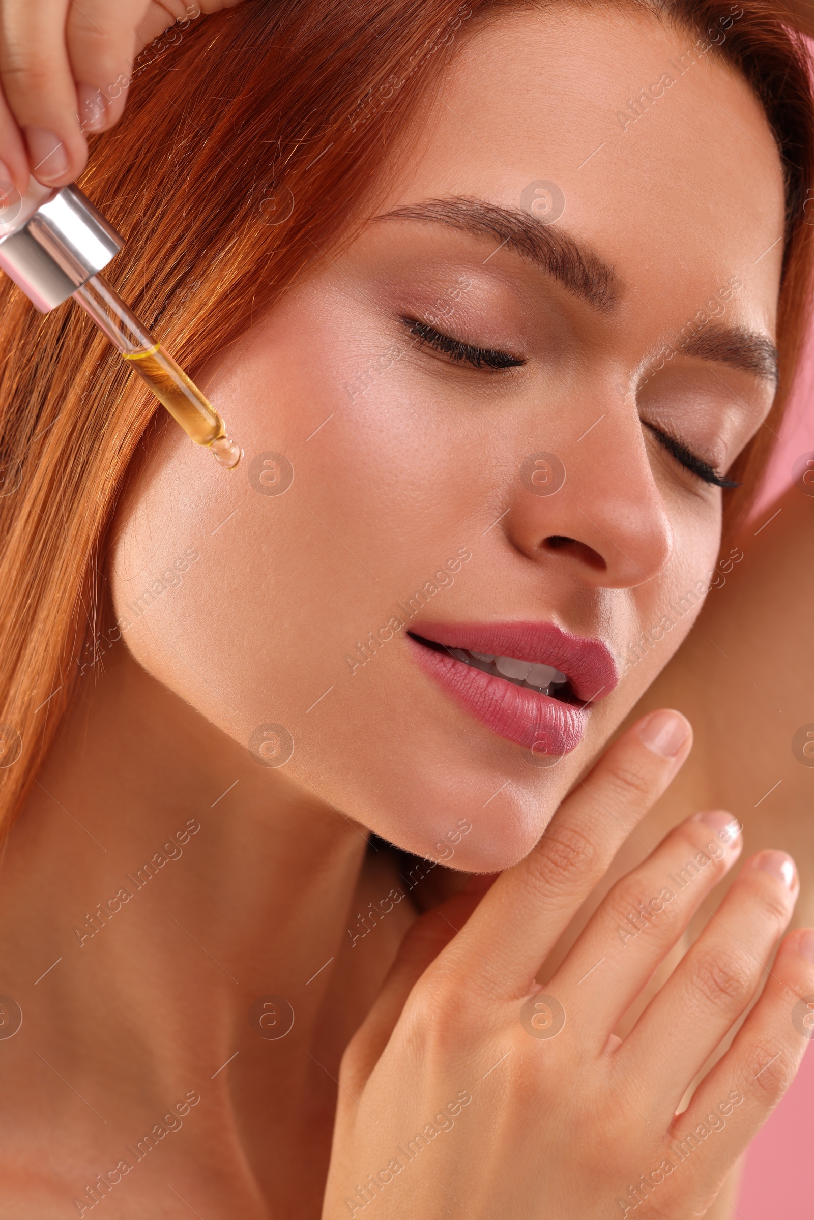Photo of Beautiful young woman applying cosmetic serum onto her face, closeup