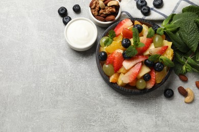 Delicious fruit salad in bowl, berries, nuts and fresh mint on grey table, flat lay. Space for text