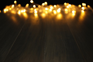 Blurred view beautiful glowing lights, focus on wooden table. Space for text