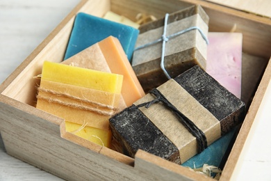 Different handmade soap bars in wooden box on table, closeup